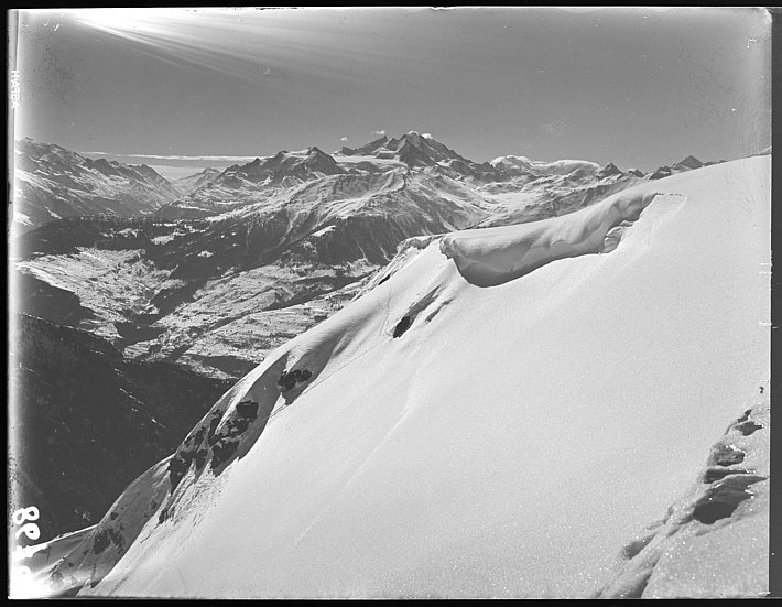 Schneebedeckter Berghang im Vordergrund mit Bergkette im Hintergrund unter klarem Himmel