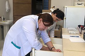 Two women in lab coats are working in a laboratory. They are cleaning drawers.