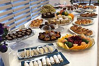The image features a long table elegantly arranged with a variety of desserts and pastries. There are trays of sweet treats, including cakes, cookies, and fruits, creating a colorful and appetizing display.