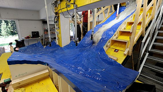Blaues, spiegelverkehrtes Modell der Region von Blatten. Von oben kommt ein Matschgemisch den künstlichen Hang herunter.