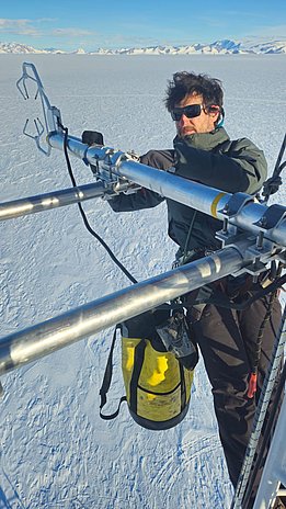 Person mit Sonnenbrille und Winterjacke stellt Turbulenzsensor an Metallgestell über schneebedeckter Landschaft ein.