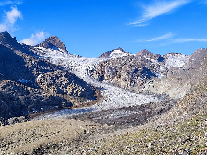 Gries Glacier in the Alps showing a visible ice field surrounded by rocky mountains under a blue sky with few clouds.