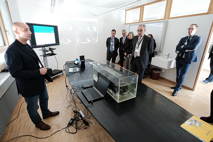 Röhrenförmiges Gerät in einem Aquarium wird von einer Gruppe Menschen betrachtet