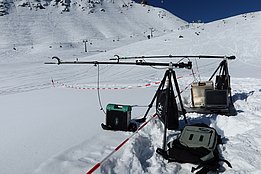 Versuchsaufbau mit Messgeräten und Laptop auf Stativ im Schnee vor verschneitem Berg mit Skilift
