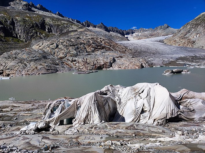 Mountain landscape with glacier, lake, and rocks, foreground ice rocks covered with white protective sheets.