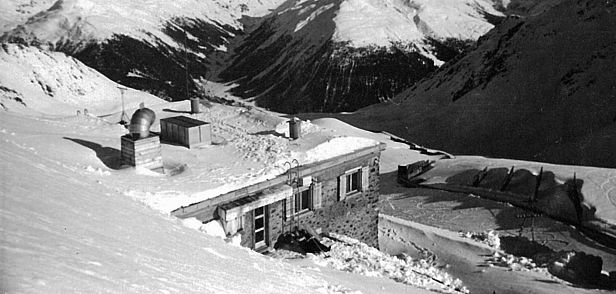 Schwarz-Weiss-Aufnahme eines steinernen Gebäudes im Schnee, mit Bergen im Hintergrund