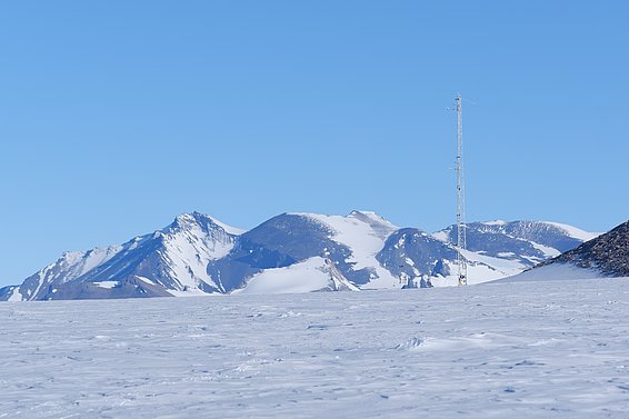 Schneebedeckte Berglandschaft unter klarem blauem Himmel mit einer hohen Messstation auf der rechten Seite