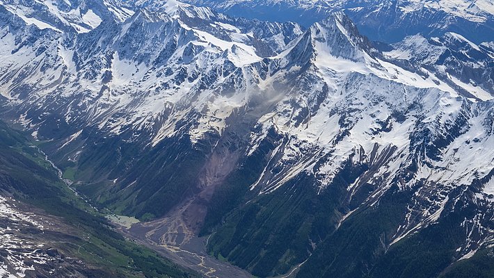 La photo montre une vue aérienne de l'éboulement de roches et de glace à Blatten, avec des sommets enneigés.