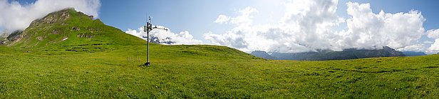 Grüne Bergwiese mit Messstation und bewölktem Himmel im Hintergrund