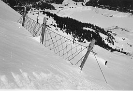 Schwarz-weißer Hang mit Schneeschutzzaun und verschneiter Berglandschaft im Hintergrund