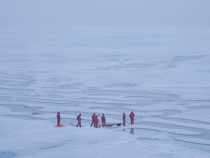 Menschen in roter Schutzkleidung auf zerklüftetem Eis mit Wasserflächen