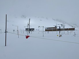Verschneites Versuchsfeld mit Messstationen und Wetterinstrumenten vor nebelverhüllten Bergen