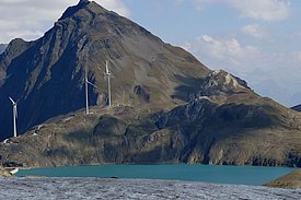 Windräder auf einem Bergkamm hinter einem schmelzenden Gletscher unter blauem Himmel mit Wolken