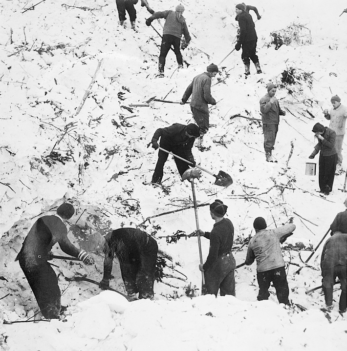 A group digs with shovels in an avalanche debris cone.