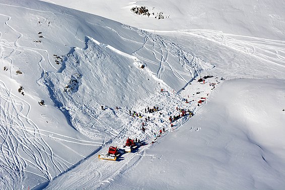 Lawinenabgang an einem schneebedeckten Berghang mit Rettungskräften und Fahrzeugen im Einsatz