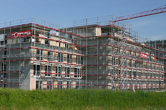 Mehrere mehrstöckige Wohngebäude in Uznach im Rohbau mit Gerüsten und Baukran, umgeben von grünem Gras