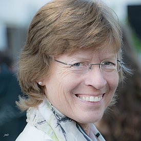 Femme aux cheveux blonds courts, portant des boucles d'oreilles en perle et un foulard clair à motif floral.