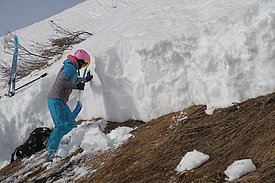 Person mit pinkem Helm, blauer Skibekleidung und Schaufel nimmt in einem Gleitschneeanriss ein Schneeprofil auf