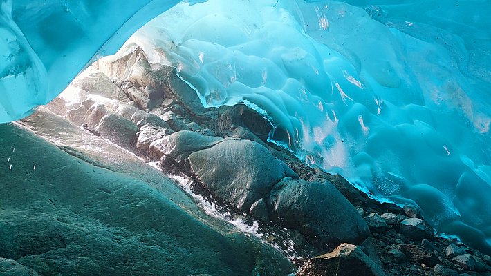 Blick aus einer Eishöhle mit glatten, bläulichen Eiswänden und Felsen am Boden