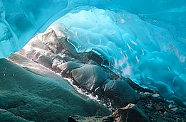 A view from inside an ice cave with smooth, bluish ice walls and rocks on the floor