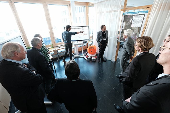 Roter Betonwürfel, Steinschlag und Menschen, die einem Redner zuhören