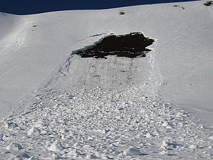 Gleitschneelawine mit abgegangener Schneeschicht und freigelegtem dunklem Boden am Berghang