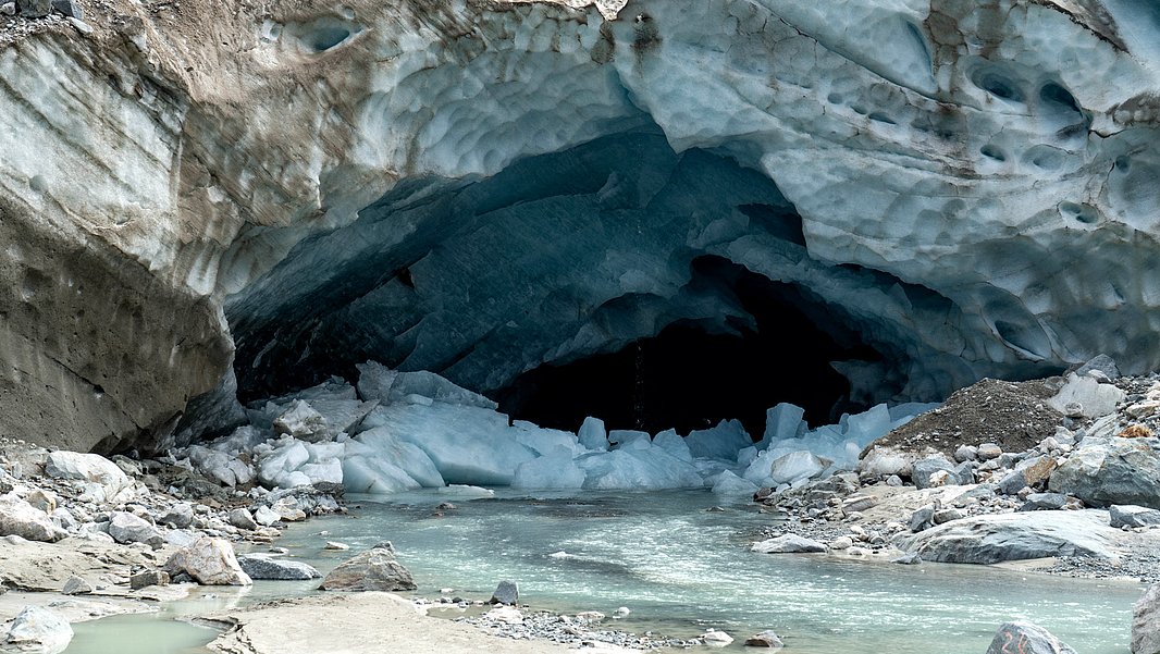 The ice cave at the Vadret da Morteratsch (GR). There are big chunks of ice and water in front of it.