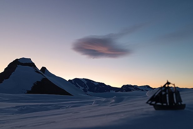 Altocumulus lenticularis Wolke über schneebedeckten Utsteinen im Dämmerlicht, mit Modellsegelschiff im Vordergrund
