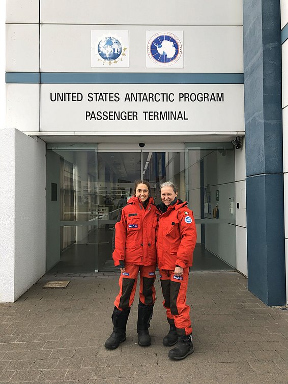 Due persone in tute da spedizione arancioni sono in piedi davanti all'ingresso del terminal passeggeri dello United States Antarctic Program a Christchurch.