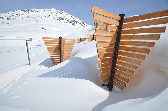 Schneeschutz aus Holz auf verschneitem Berg mit blauem Himmel