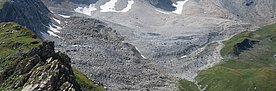 Blockgletscher oberhalb der Alp Flix. Der Blockgletscher selbst sieht aus wie eine Geröllhalde. Allerdings wird das Gestein durch die Vergletscherung so befestigt,  dass die Neigungswinkel viel steiler sind als bei lockerem, frei liegendem Geröll. Der grau-beige Blockgletscher ist links und rechts von grünen Hängen eingerahmt.